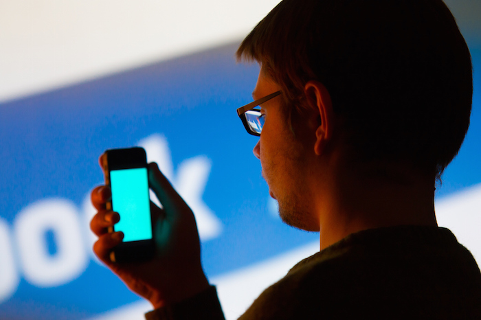 Man using Facebook application on smartphone - studio shoot on backround image from the projector